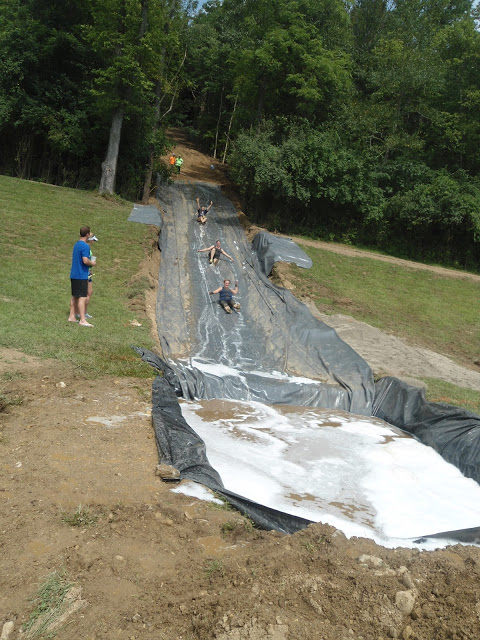 Image of obstacle course racers sliding down a massive tarp waterslide at the Mud Guts and Glory race course