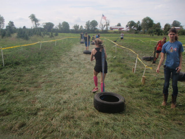 Image of athlete dragging a tire attached to a firehouse down a grassy field during the 2012 Hero Rush Obstacle Course Race