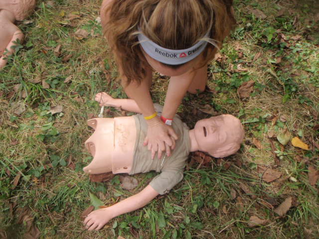 Woman performs CPS on a small dummy in the grass during the 2012 Hero Rush Obstacle Course Race