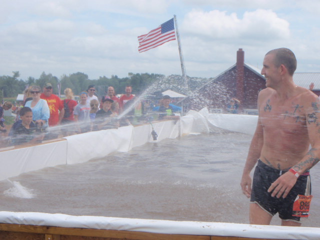 Geoffrey Hart walks through a large pool while children aim fire hoses squirting water at him, during an obstacle at the 2012 Hero Rush Obstacle Course Race