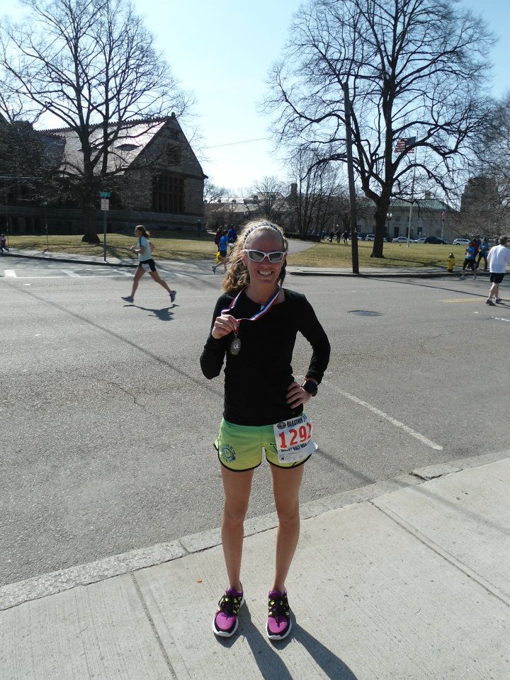 Heather Hart smiling at the finish of the Quincy Half Marathon holding up her medal