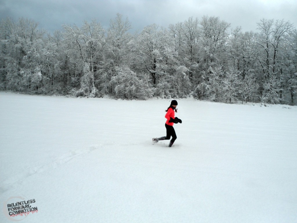Image of Heather Hart running through deep snow, with snow covered trees in the background 