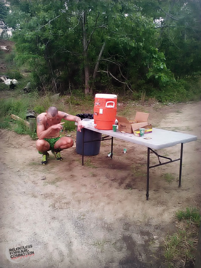Photo of Geoffrey Hart bent over in front of an ultramarathon aid station table, unable to take in any more fuel or water due to palate fatigue 