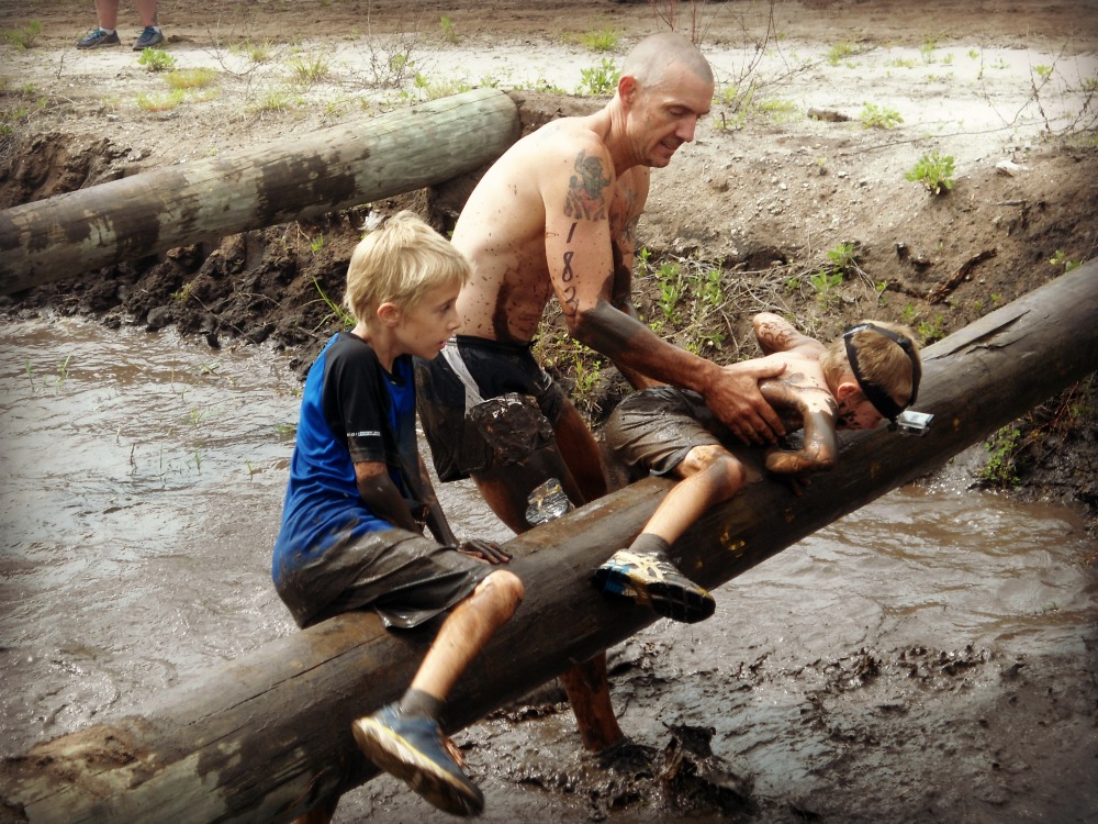 Father helps son over log during a mud run obstacle course race