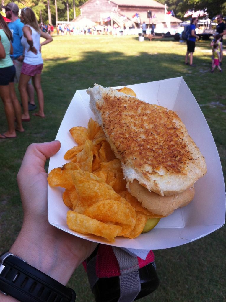 Image of a runner hand holding a water bottle and a grilled cheese sandwich before a race