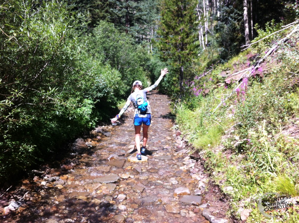 Heather hart tip toeing down a stream through the middle of a forest during the TransRockies Run 6 Day Stage Race event in Colorado