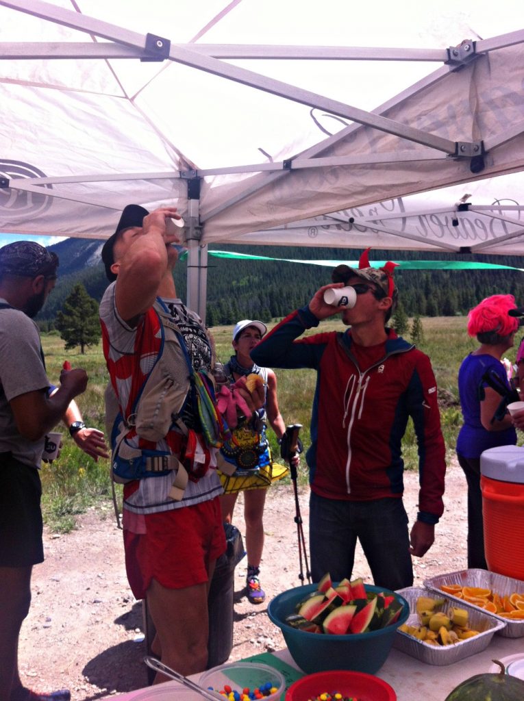 Geoff Hart and Ultrarunner Max King taking shots from paper cups at an aid station table during the 2016 TransRockies 6 day stage run