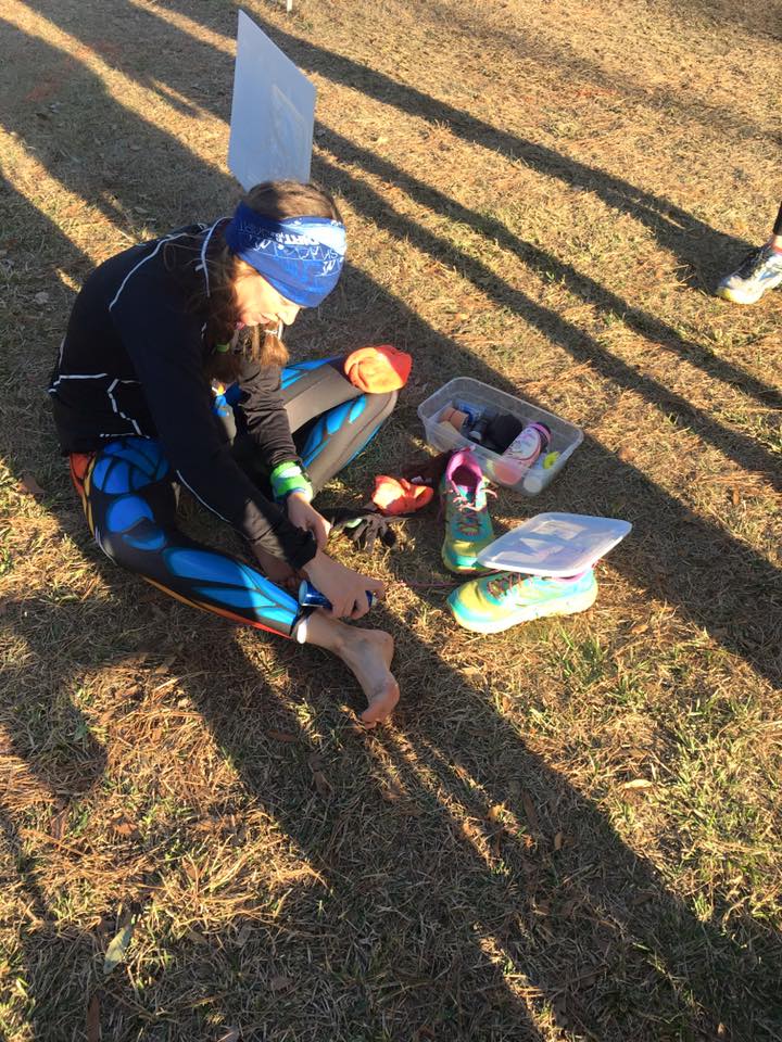 Heather Hart sitting on the ground fixing her feet during a looped ultramarathon course