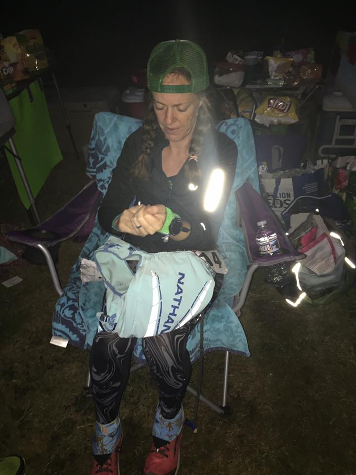 Ultrarunner sitting in a chair adjusting her watch during the overnight portion of a 100 mile ultramarathon