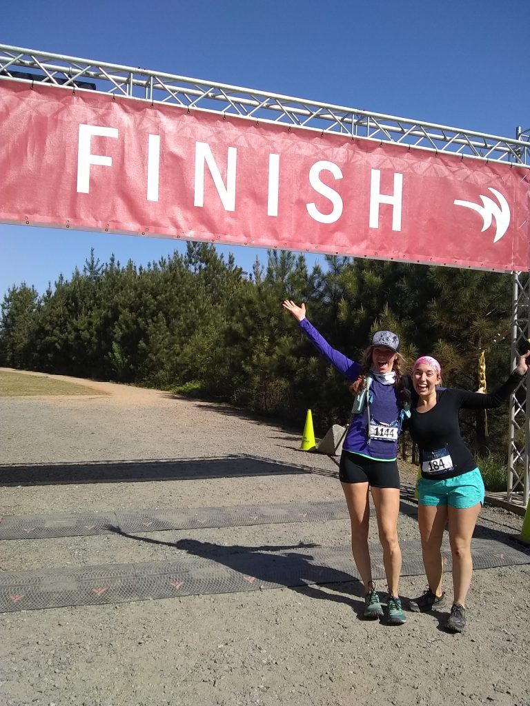 Two female runners smiling and celebrating at the finish line of a running race