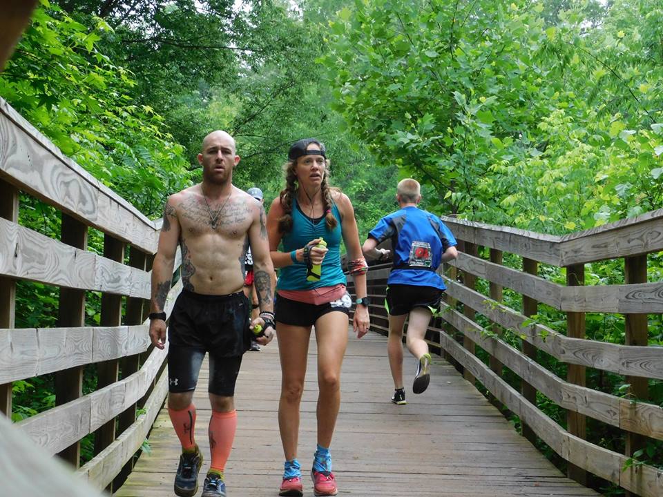 Heather Hart walking across a bridge with a fellow male runner looking exhausted, about 70 miles in to a 100 mile ultramarathon 