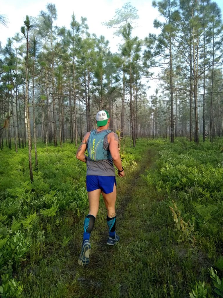 photo of a trail runner running down a lush, green, single track trail 