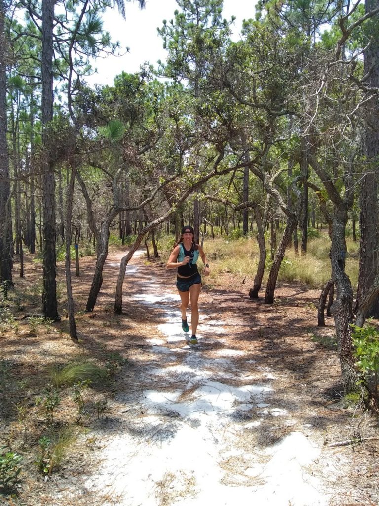 Heather Hart trail running down a sandy trail at Carolina Beach State park