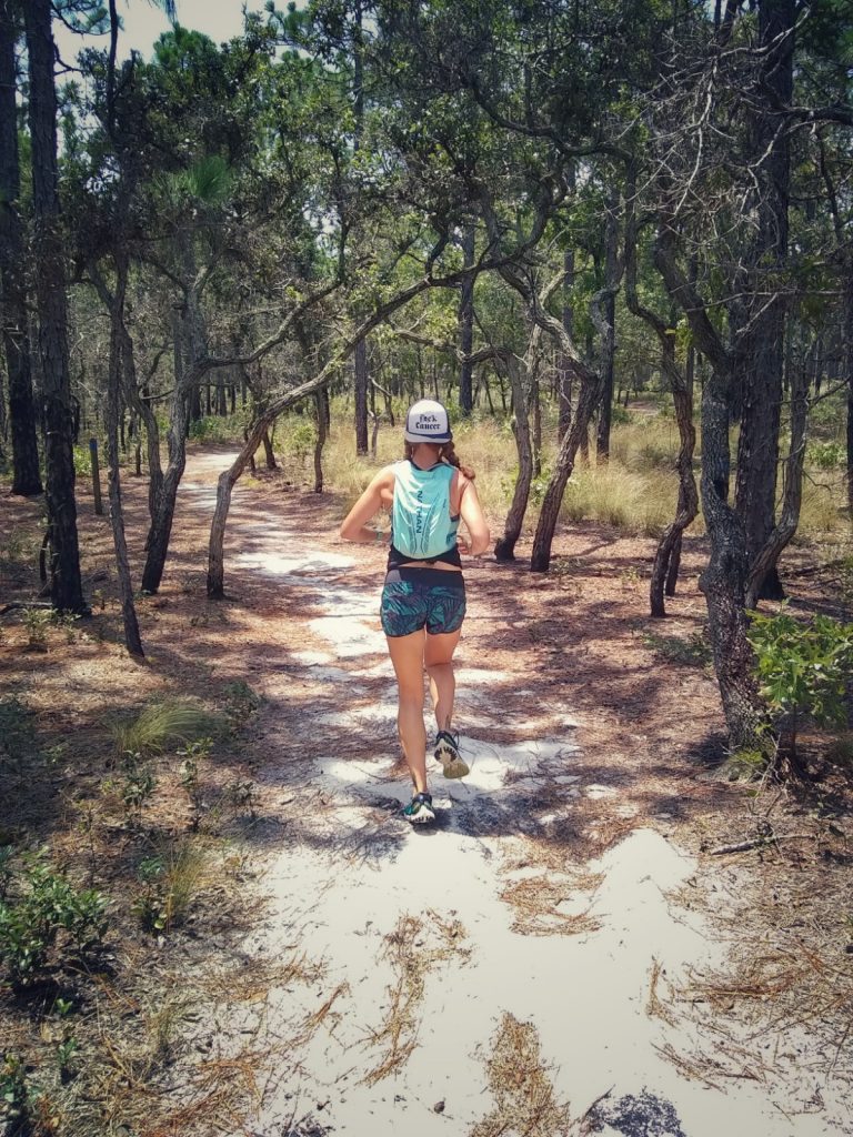 Heather Hart running down a sandy, coastal carolina trail, following Trail Running Etiquette Rules by staying on the designated trail

