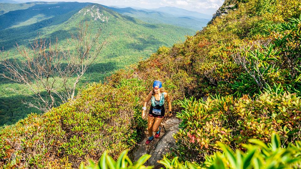 Heather Hart running down a trail over a mountain top with moutains in the background 