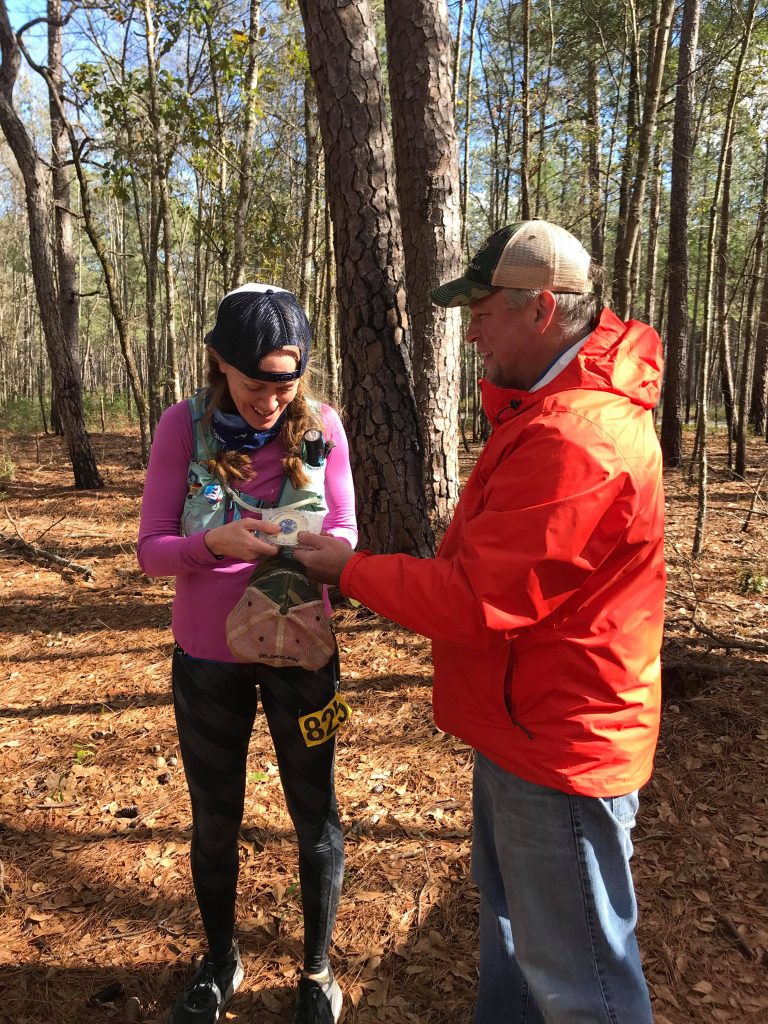 Heather Hart at a 100 mile finish line receiving her belt buckle from the race director