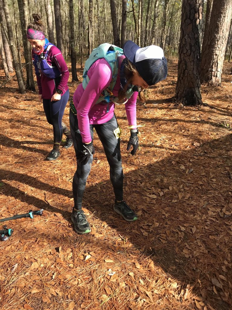 female ultramarathon runner bent over in exhaustion at the waist looking at the pine needle covered ground