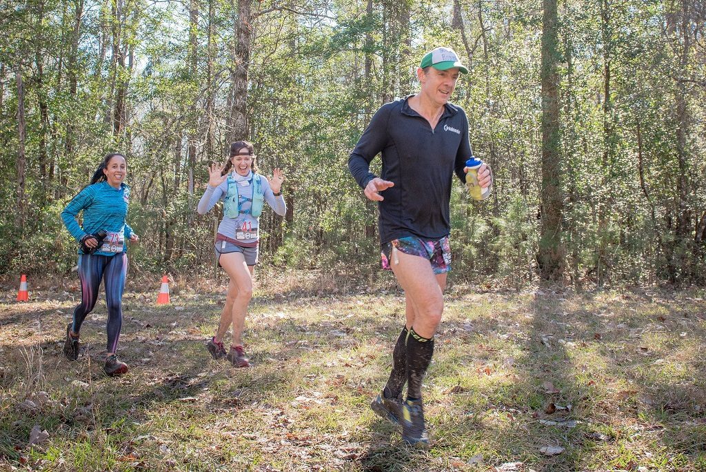 three ultrarunners running down the trail, while smiling and waving during a race