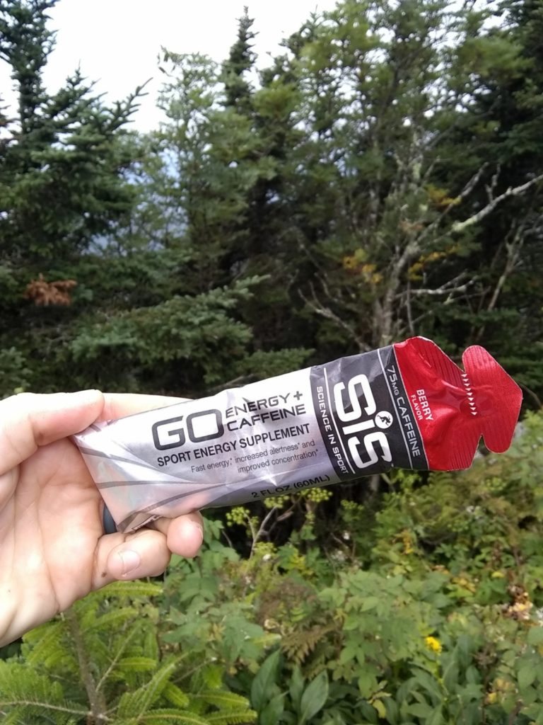 Photo of an SIS energy gel for endurance athletes, held in a hand with trees and plants in the background