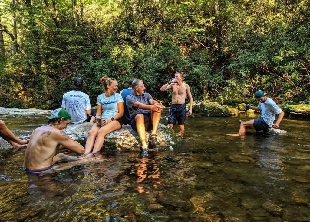 Group of runners sitting on rocks in a stream in the middle of the forest after a group run 
