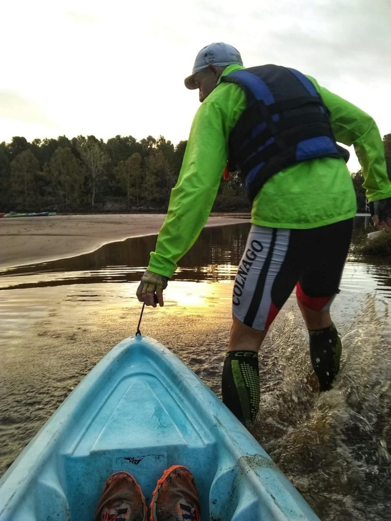 Adventure racer pulling a kayak into the water during a race