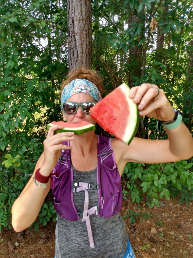 ultrarunner wearing hydration vest eating watermelon held in both hands