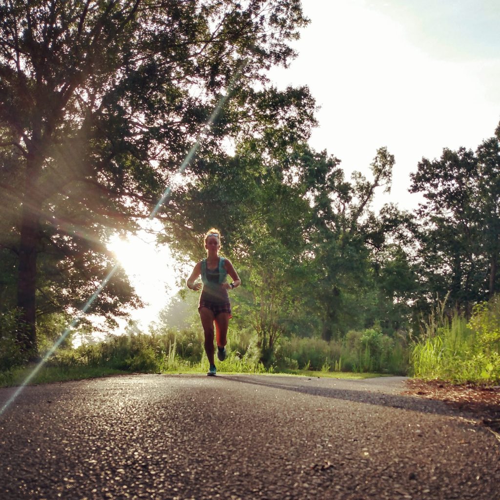 Female runner running on a paved path as the sun rises behind her