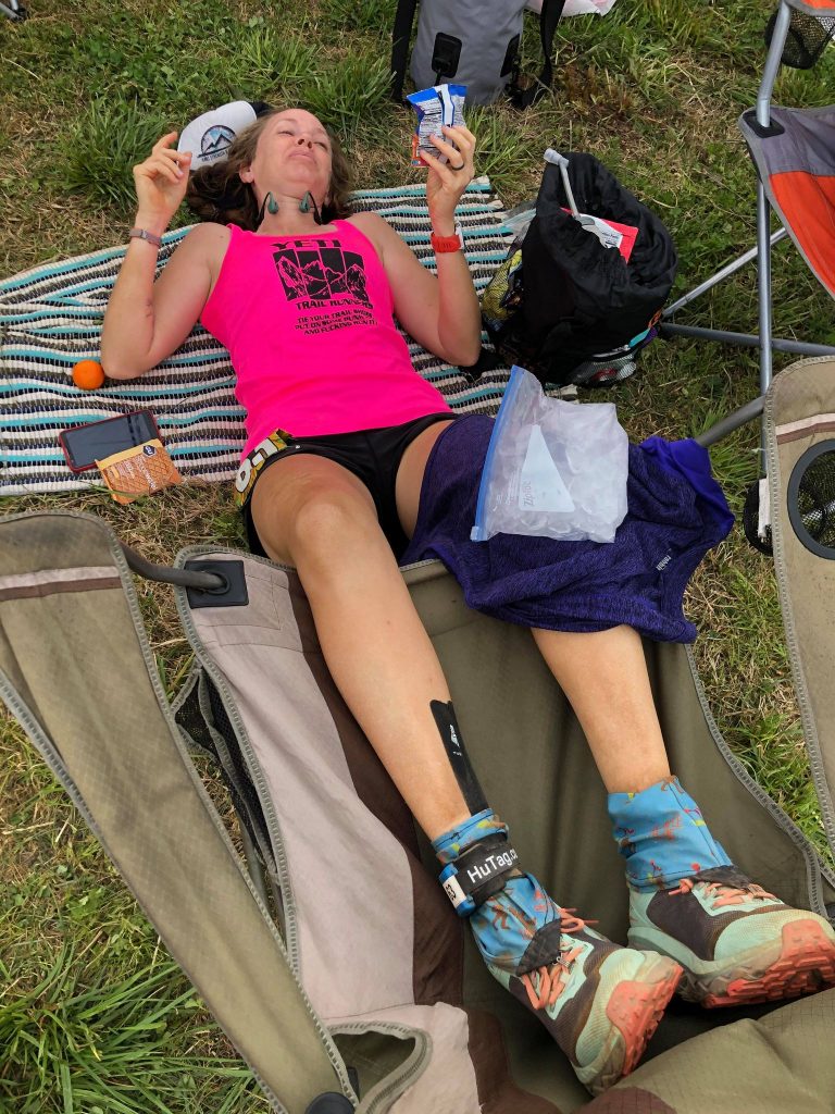 Ultrarunner laying on the ground icing her knee eating snacks during a 100 mile ultramarathon