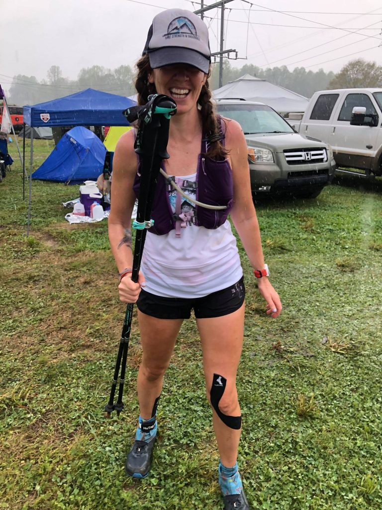 Heather Hart smiling in the rain, holding trekking poles and wearing a COROS APEX 46mm GPS watch in the middle of the Country Mile 100 mile ultramarathon
