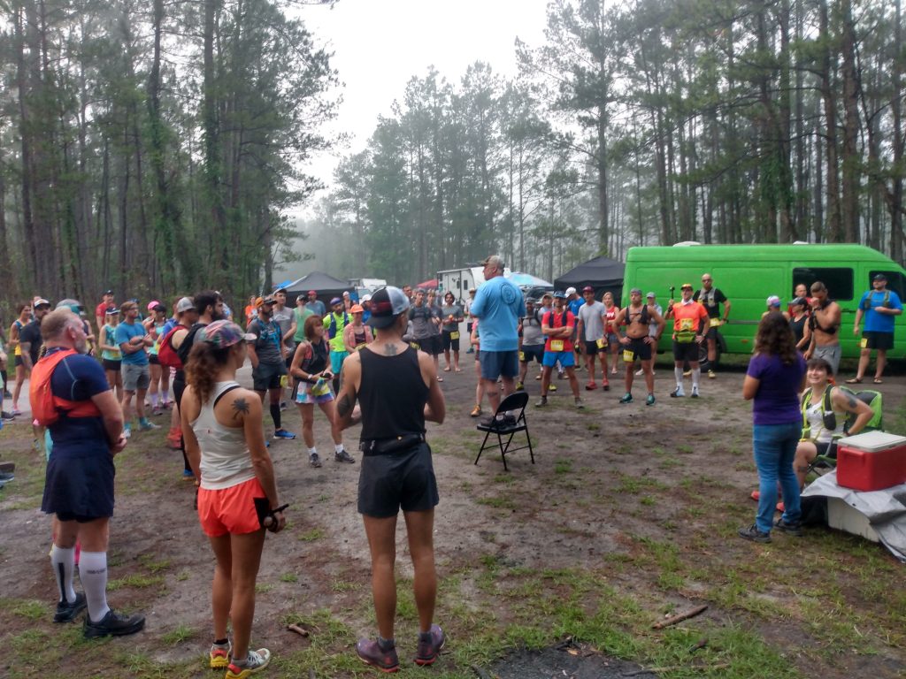 Large crowd around the race director in the woods at the starting line of the Hell Hole Hundred and other ultramarathon distances 