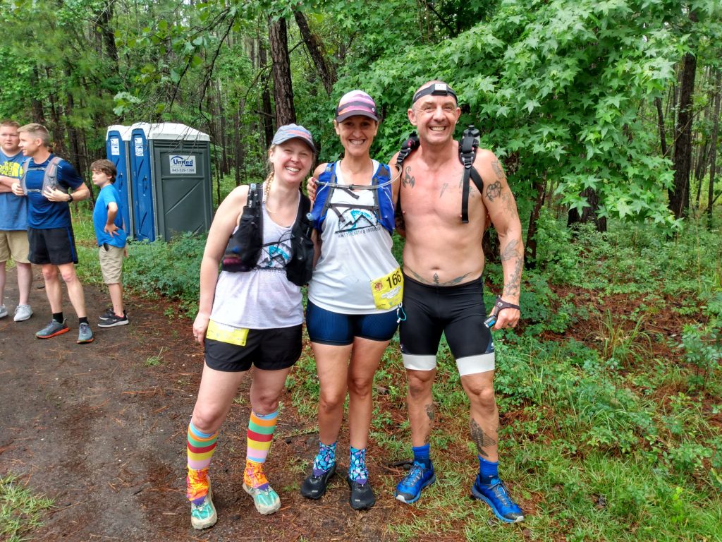Geoffrey Hart posing with two ultramarathon coaching clients in the woods before the start of a trail race