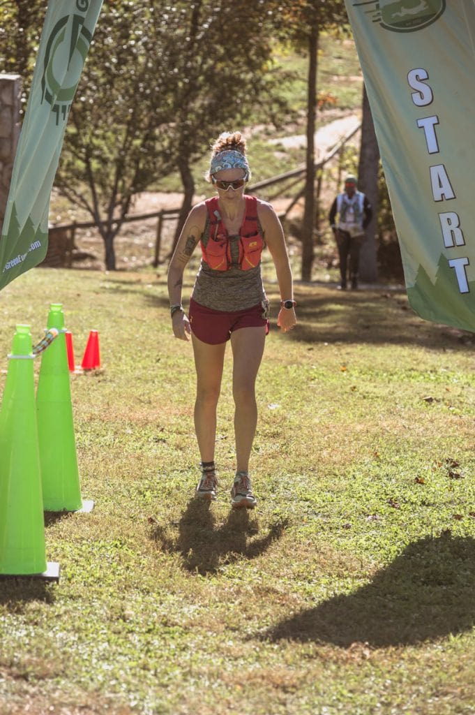 Ultramarathon runner Heather Hart walking across a start/finish line looking fatigued