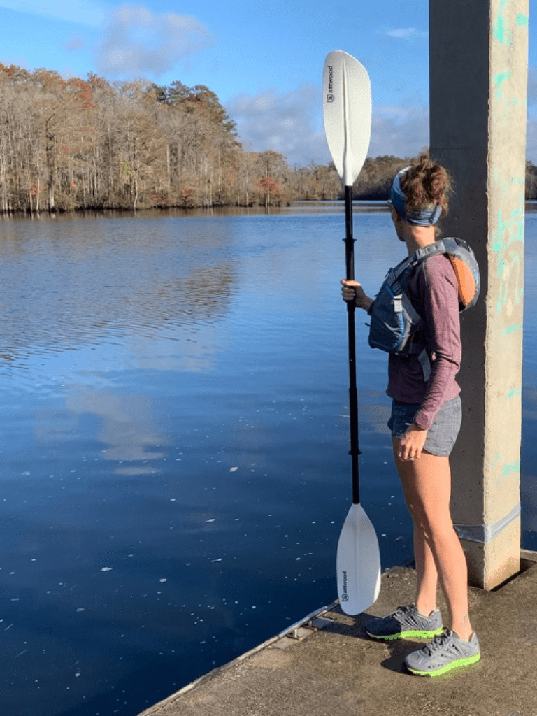 Heather Hart standing on a boat dock over a river wearing CrossKix APX Hybrid Footwear holding paddle