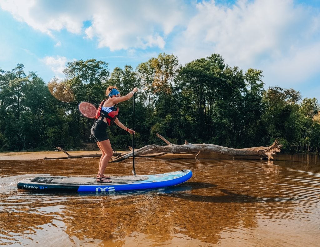 Woman stand up paddle boarding on a river near the shoreline