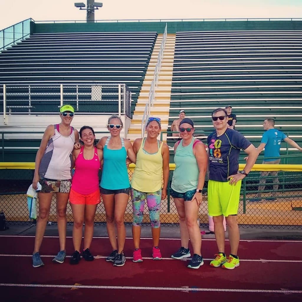 A group of runners wearing colorful clothing posing together on a track before running practice