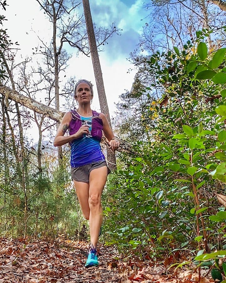 Trail and ultrarunner Heather Hart running down a trail in the forest covered in leaves