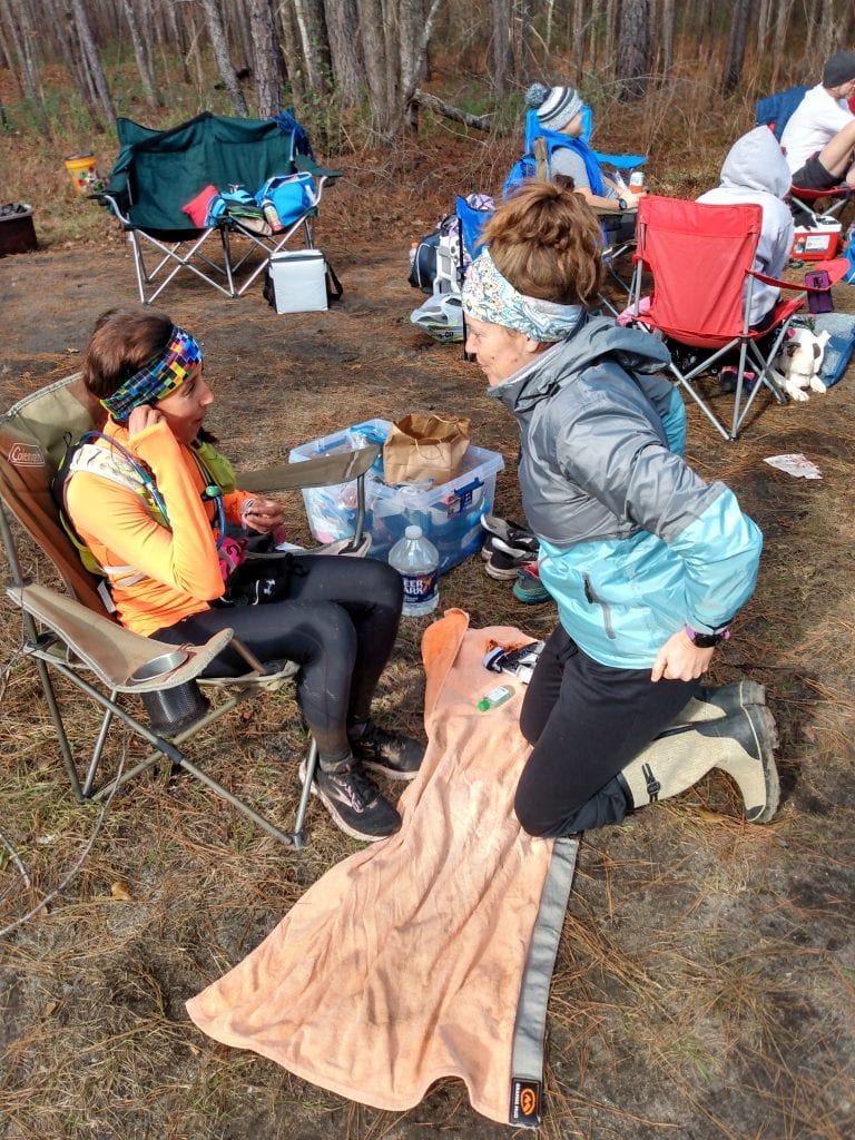 Heather Hart talking to one of her ultramarathon coaching clients during a 100 mile race.  Female runner is sitting in chair getting ready to change shoes during the race. 