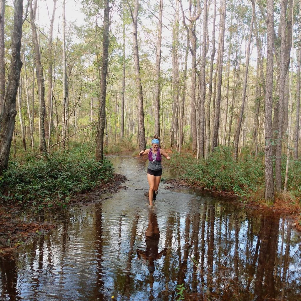 Woman running down a flooded trail in the forest
