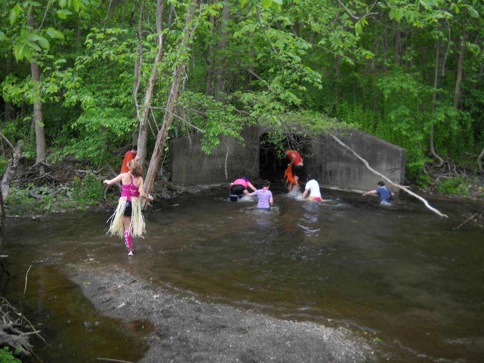 Image of Hashers running through water and heading into a tunnel in the forest. 