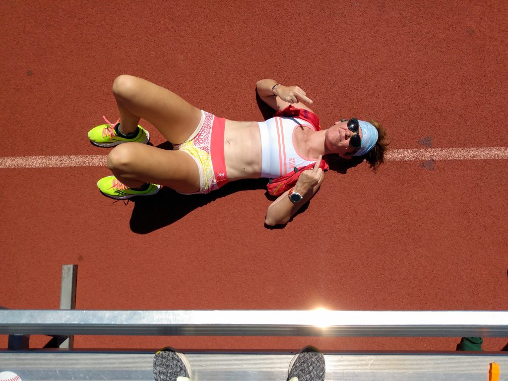 woman laying on a red rubber track and field track exhausted after running 