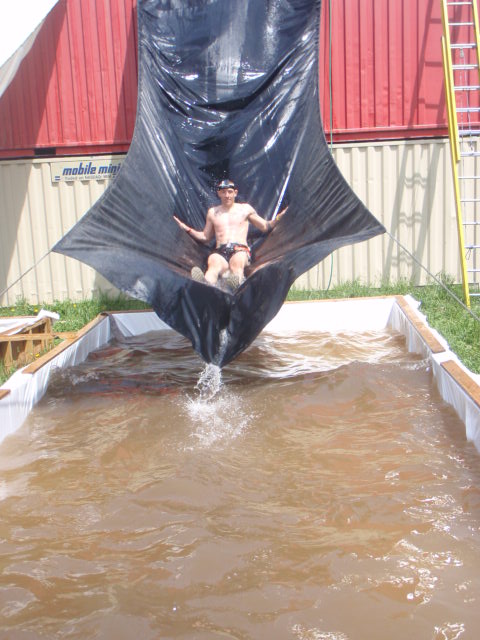 Geoffrey Hart slides down giant plastic tarp, coming off of shipping containers into a pool of water at the the Hero Rush OCR