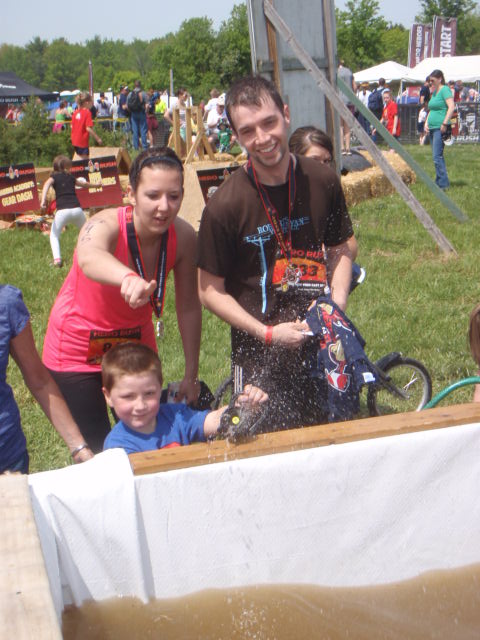Two athletes help a younger child shoot a firehose at the the Hero Rush OCR