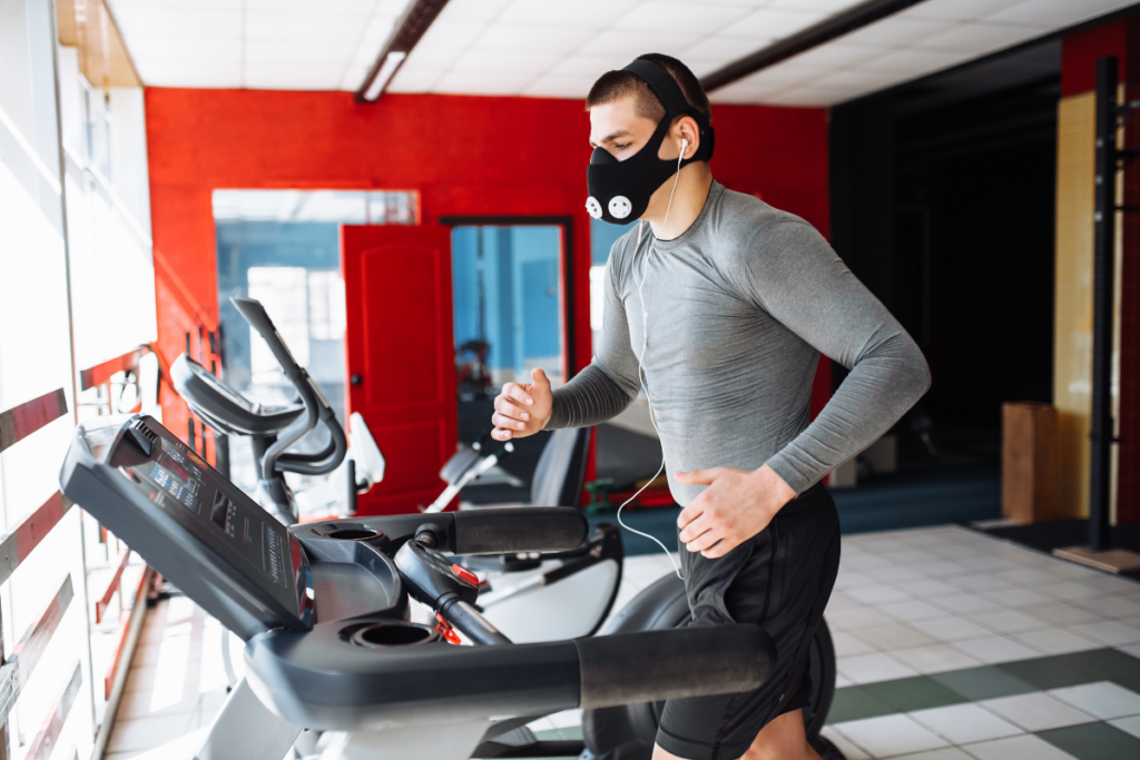 Man runs on a treadmill in a gym wearing an altitude training mask