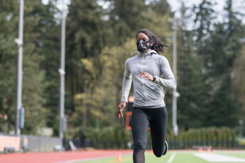 Woman sprints outdoors on a track wearing an elevation training mask