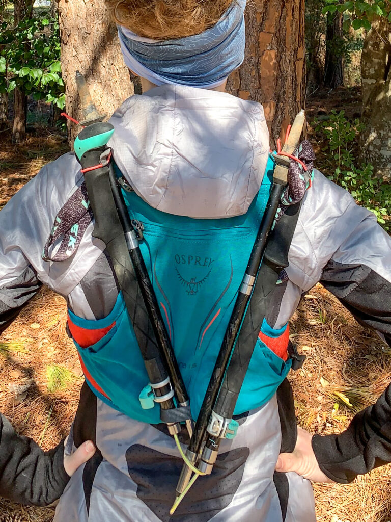 trail runner showing hydration pack with trekking poles strapped to the back