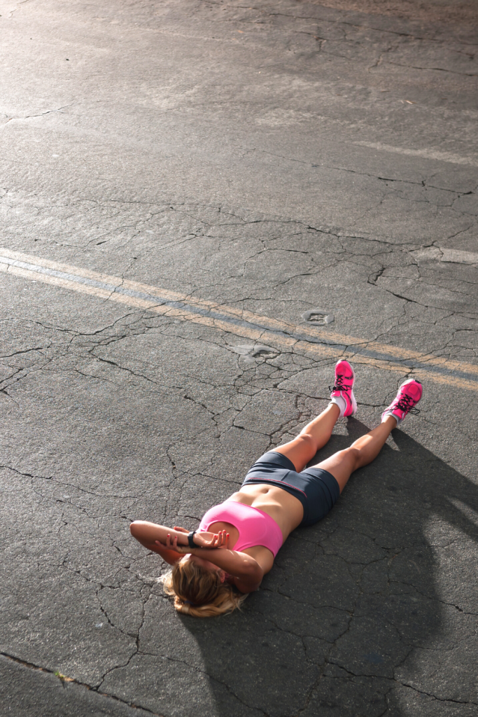 woman lays on the pavement exhausted after running 