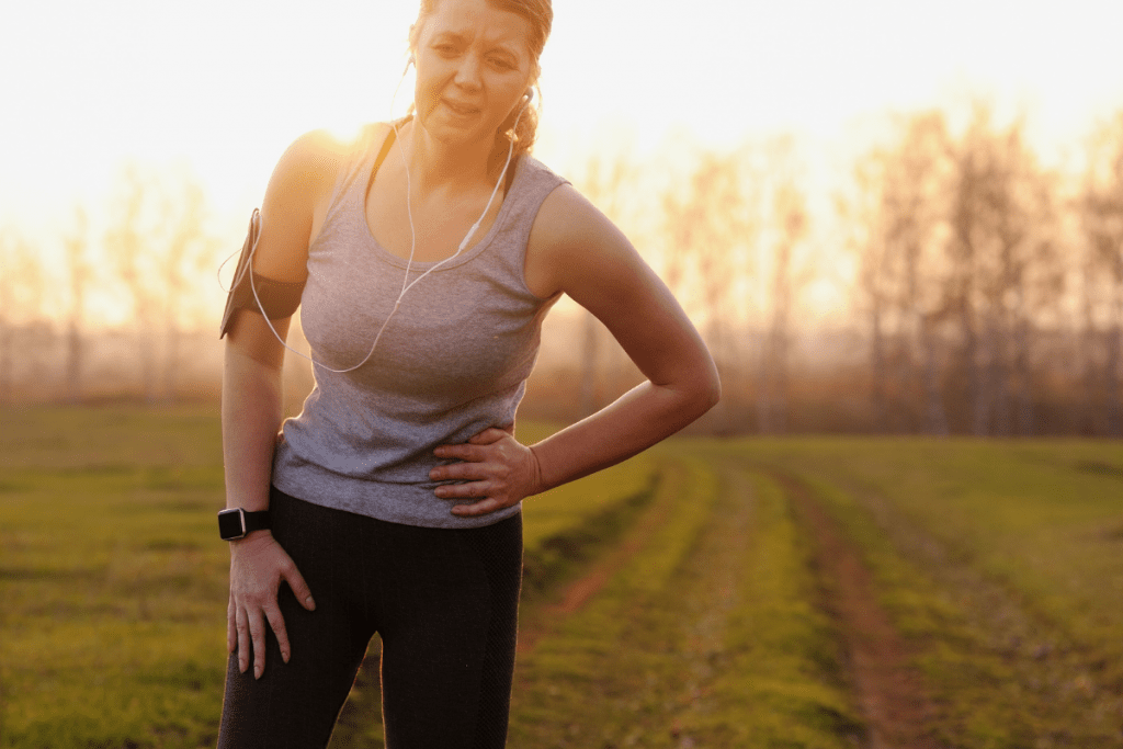 Side stitches when running is a pain no runner wants to experience.  Woman standing in a field holding her side in pain during the middle of a run. 
