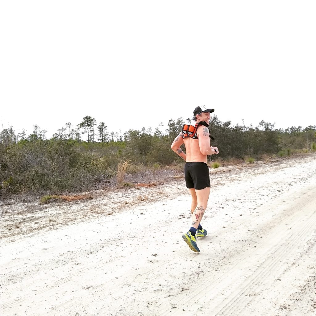 Geoff Hart running down a dirt road wearing an orange mud backpack 