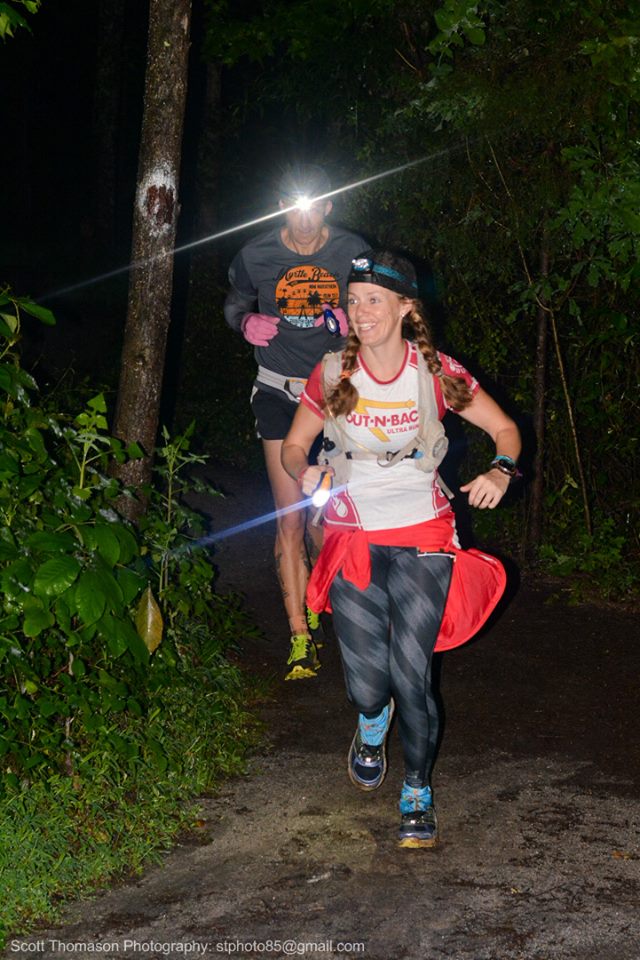 Ultramarathon runners wearing headlamps and carrying lights while running on a trail in the dark 