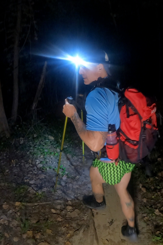Geoffrey Hart hiking through the woods at night wearing a running headlamp on his forehead